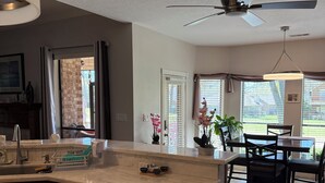 A modern kitchen with a central island, a dining area with a table and chairs, and a ceiling fan. - 3-bedroom golf course home on Walden on Lake Conroe Montgomery with WiFi, AC (Montgomery)