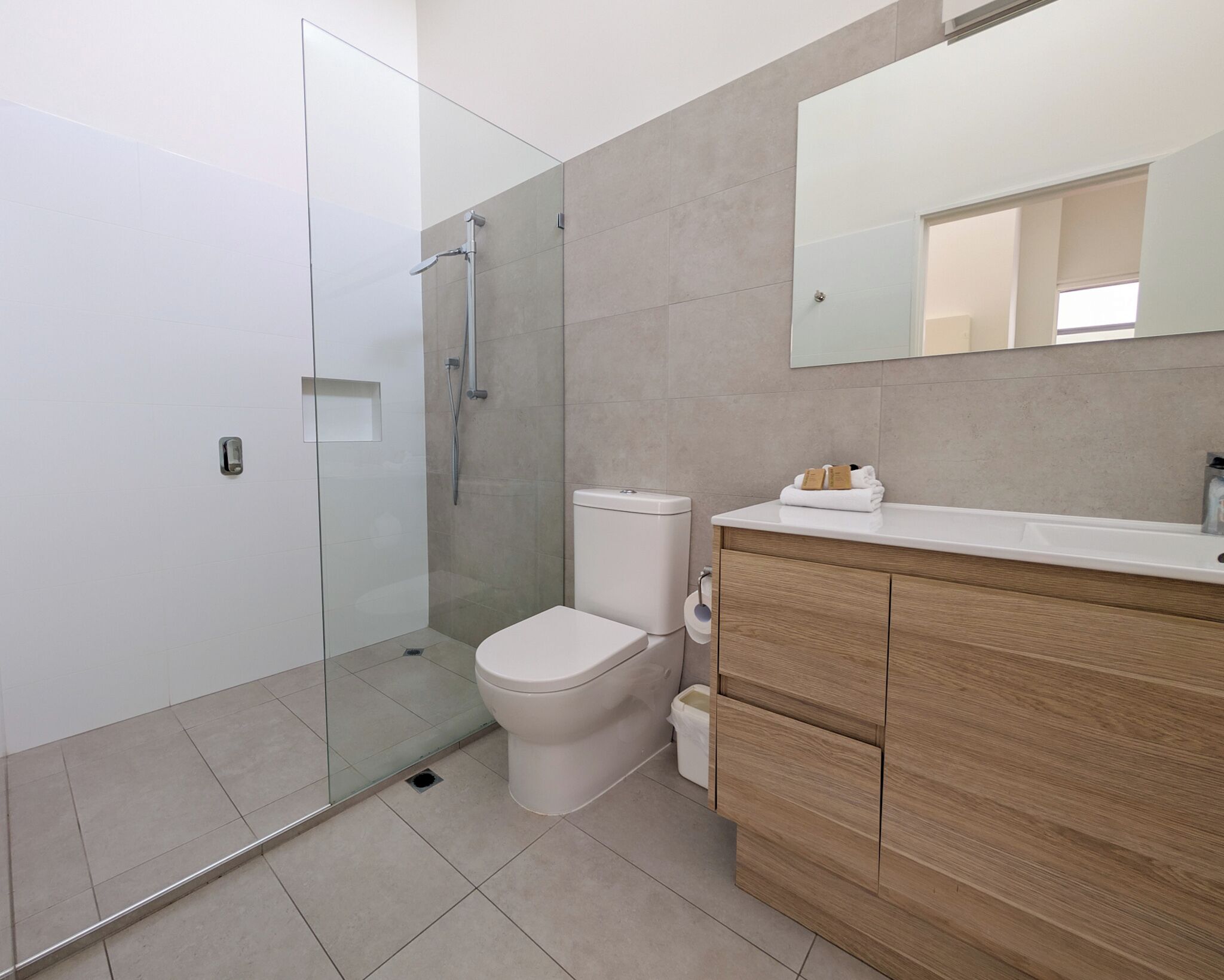 Un baño moderno con ducha de vidrio, inodoro blanco y tocador de madera con espejo.