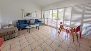 A living room with a sofa, coffee table, and dining table with chairs. - Noosa Parade Holiday Inn (Noosa Heads)