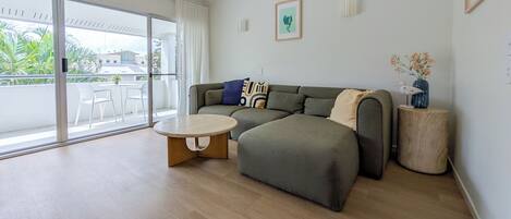 Un salon moderne avec un canapé, une table basse ronde et une vue sur un balcon aménagé avec du mobilier d’extérieur.