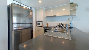 A modern kitchen with a stainless steel refrigerator, a microwave, a stove, and a sink with a stainless steel countertop. - Noosa Parade Holiday Inn (Noosa Heads)