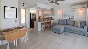 A modern living room with a grey sofa, a glass coffee table, and a dining area with a wooden table and chairs. - Noosa Parade Holiday Inn (Noosa Heads)