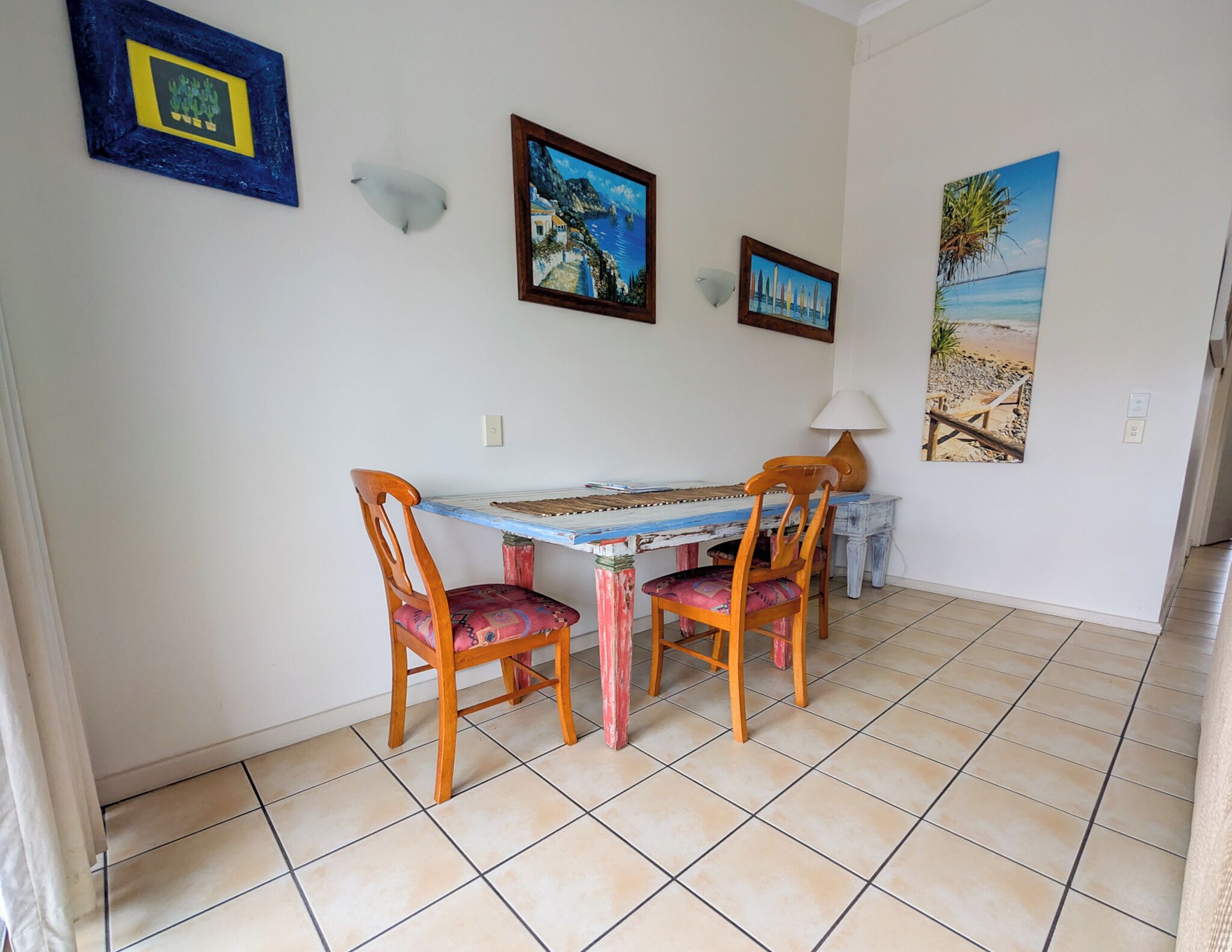 Un comedor con una mesa, sillas, una lámpara y tres cuadros en la pared.