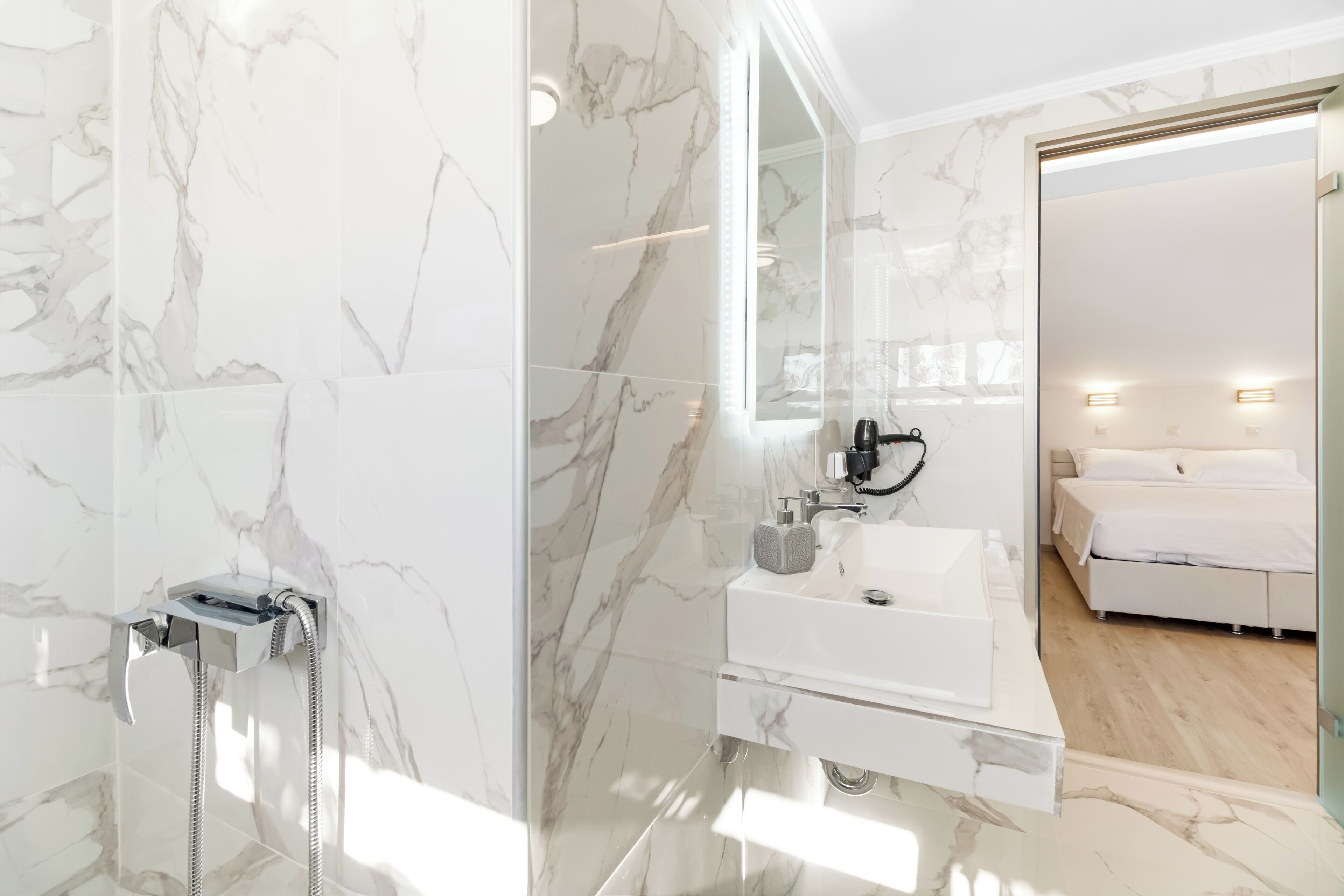 A modern bathroom with a marble shower, a white sink, and a large mirror.