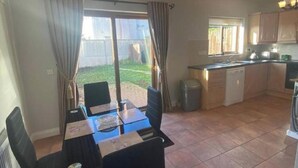 Un comedor con mesa y sillas, una cocina con armarios y un lavaplatos, y un ventanal corredizo que da a un patio.