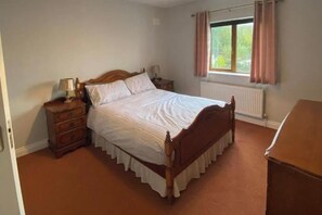 Een slaapkamer met een houten bed, nachtkastje, kledingkast en een raam met gordijnen.