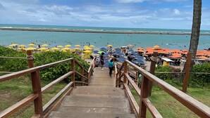 A wooden staircase leading to a beach area with umbrellas and people. - Beachfront resort Muro Alto/Porto de Galinhas, smart apartment with pool, 4-star (Ipojuca)