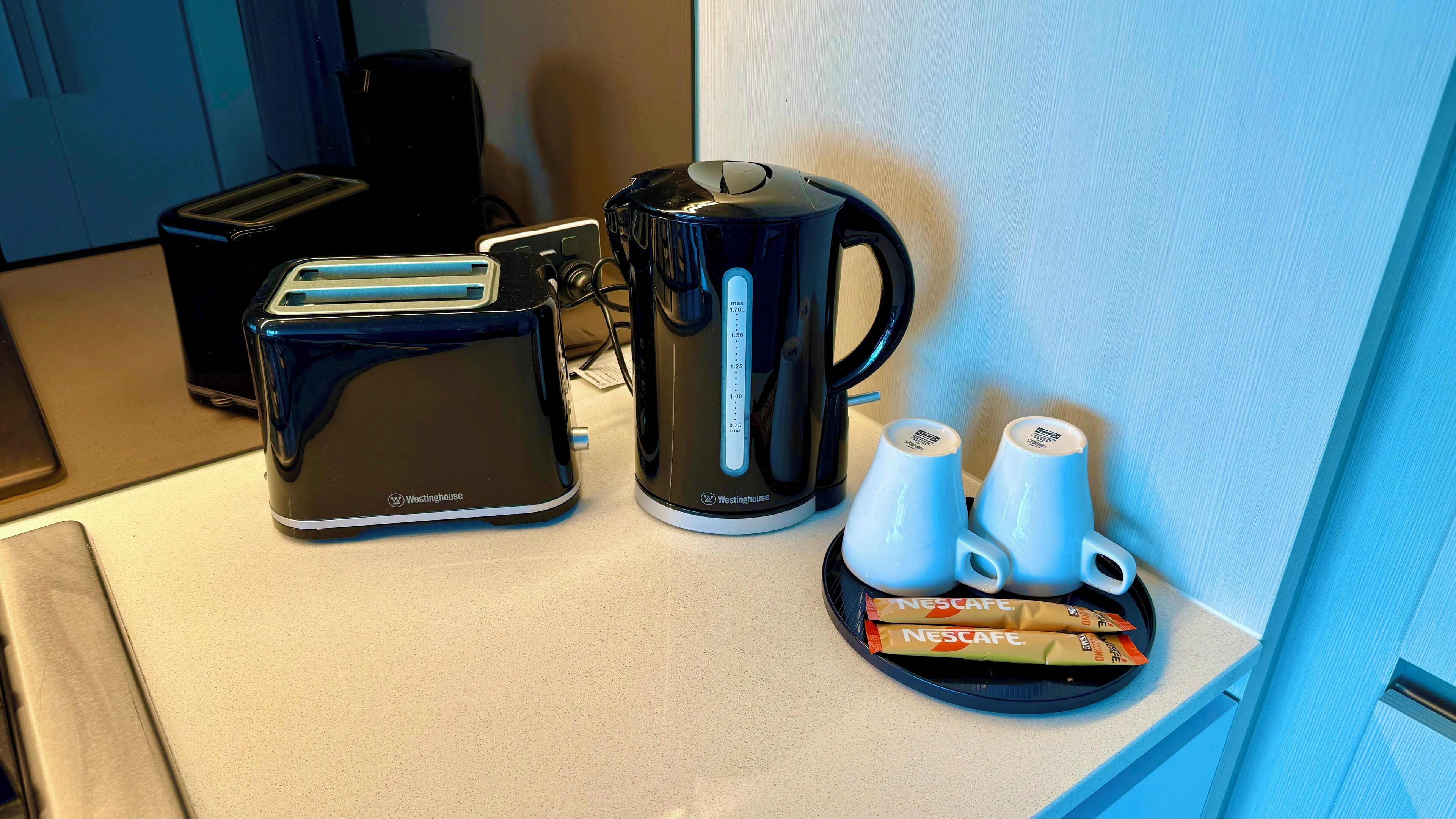 Una encimera de cocina con un tostador, una cafetera y dos tazas de Nescafé.