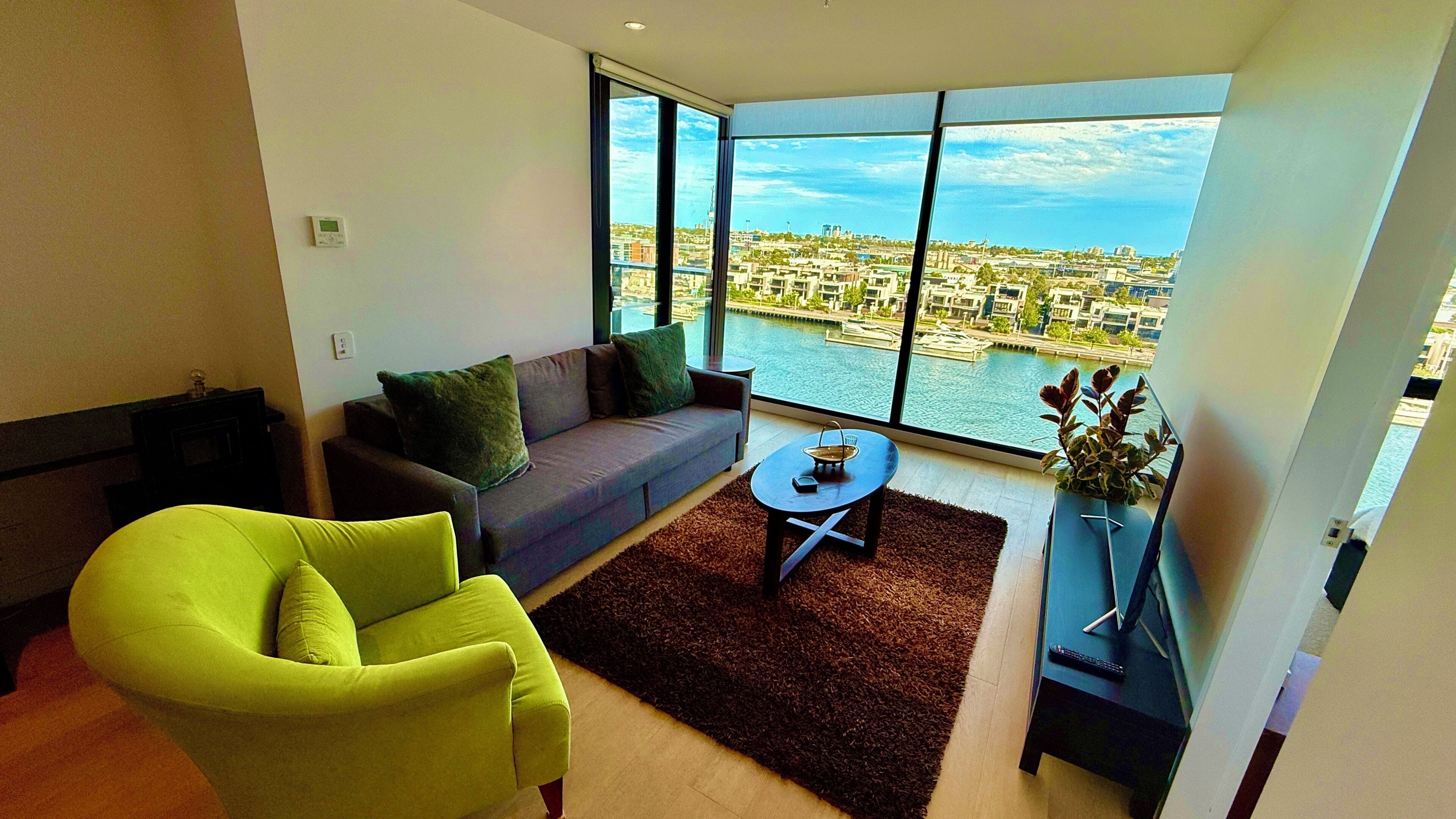 Una sala de estar moderna con sofá, sillón y vistas a un paisaje urbano a través de amplios ventanales.