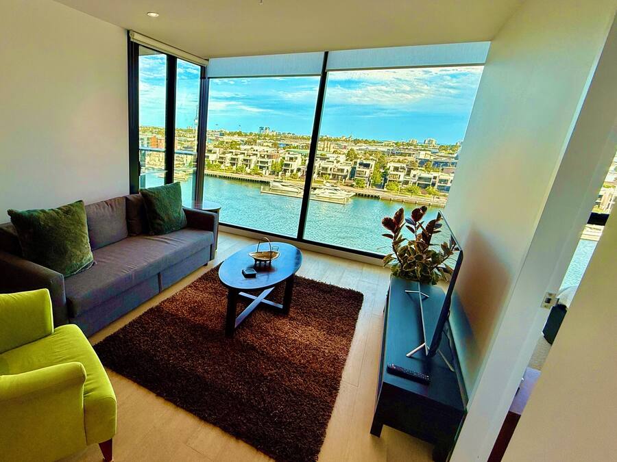 Una sala de estar moderna con sofá, sillón y vistas a un paisaje urbano a través de amplios ventanales.