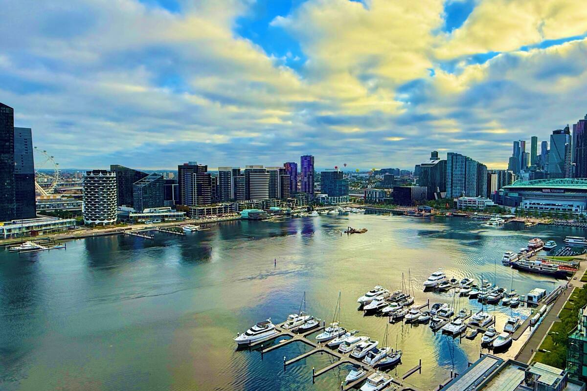 A marina with boats docked, surrounded by modern high-rise buildings and a waterfront promenade.