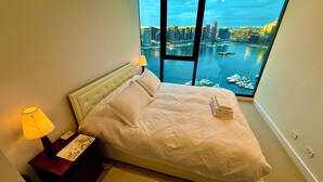 A bedroom with a large window overlooking a marina and city skyline. - Yarra Accommodation  (Melbourne)