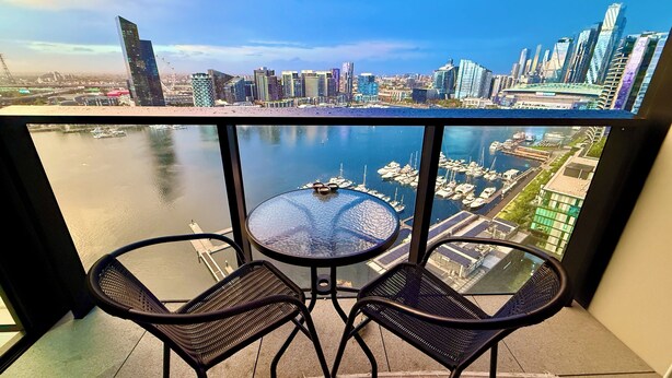 A balcony with two chairs and a table overlooking a marina with boats and a city skyline. - Yarra Accommodation  (Melbourne)