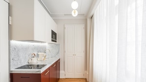 A narrow kitchen with a marble countertop, a kettle, and a coffee maker. There is a wooden cabinet and a white door in the background. - GuestReady - Downtown City Apartments - 2L (Porto)