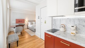 Una habitación de hotel compacta con kitchenette, cama, escritorio y una silla.