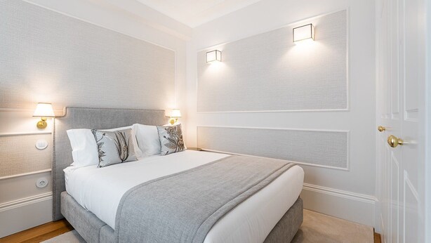 Un dormitorio ordenado con una cama grande, dos mesitas de noche e iluminación en la pared.