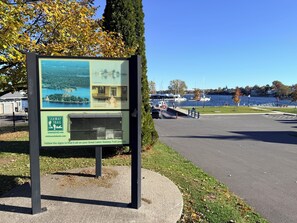 Un letrero muestra una vista panorámica de un lago y botes, un paseo pavimentado y una zona verde con bancos.