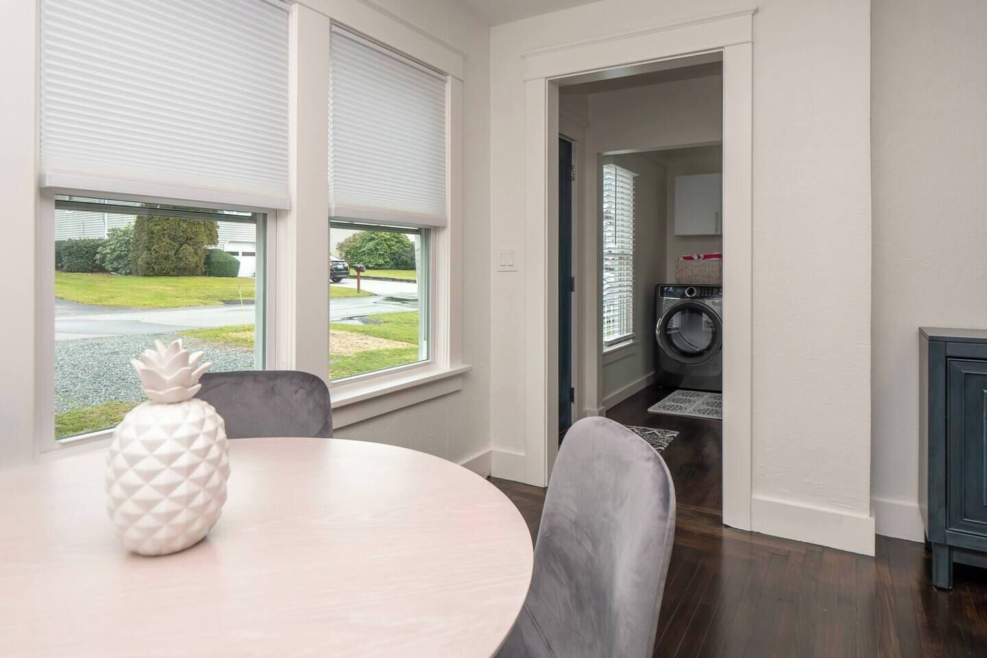 A room with a round table, a pineapple decoration, and a view of a laundry area through an open door.