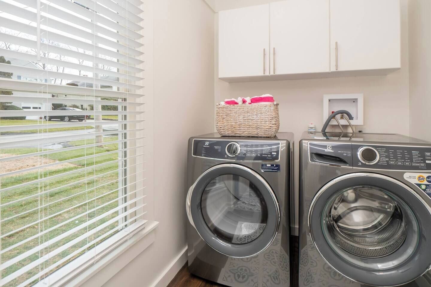 A laundry area with two front-loading washing machines, a basket of laundry, and a cabinet above.