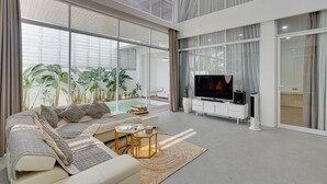 A modern living room with a large sofa, a TV, and a pool area. -  Villa Osmanthus - Kerobokan (Kerobokan)