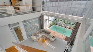 A multi-level interior with a living area featuring a sofa, coffee table, and a view of a swimming pool. -  Villa Osmanthus - Kerobokan (Kerobokan)