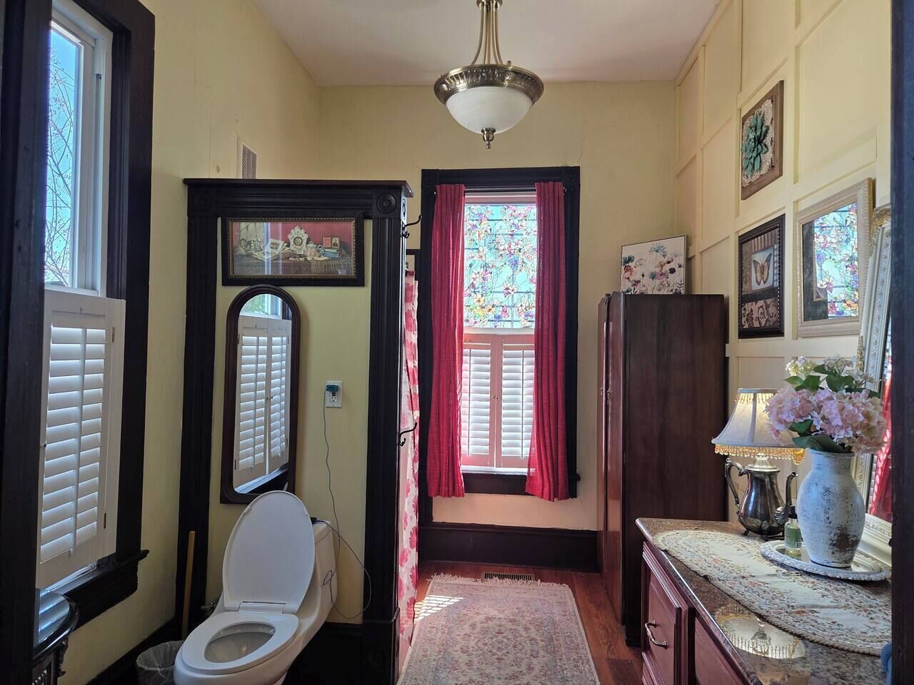 A traditional bathroom with a toilet, a mirror, and a window with red curtains.