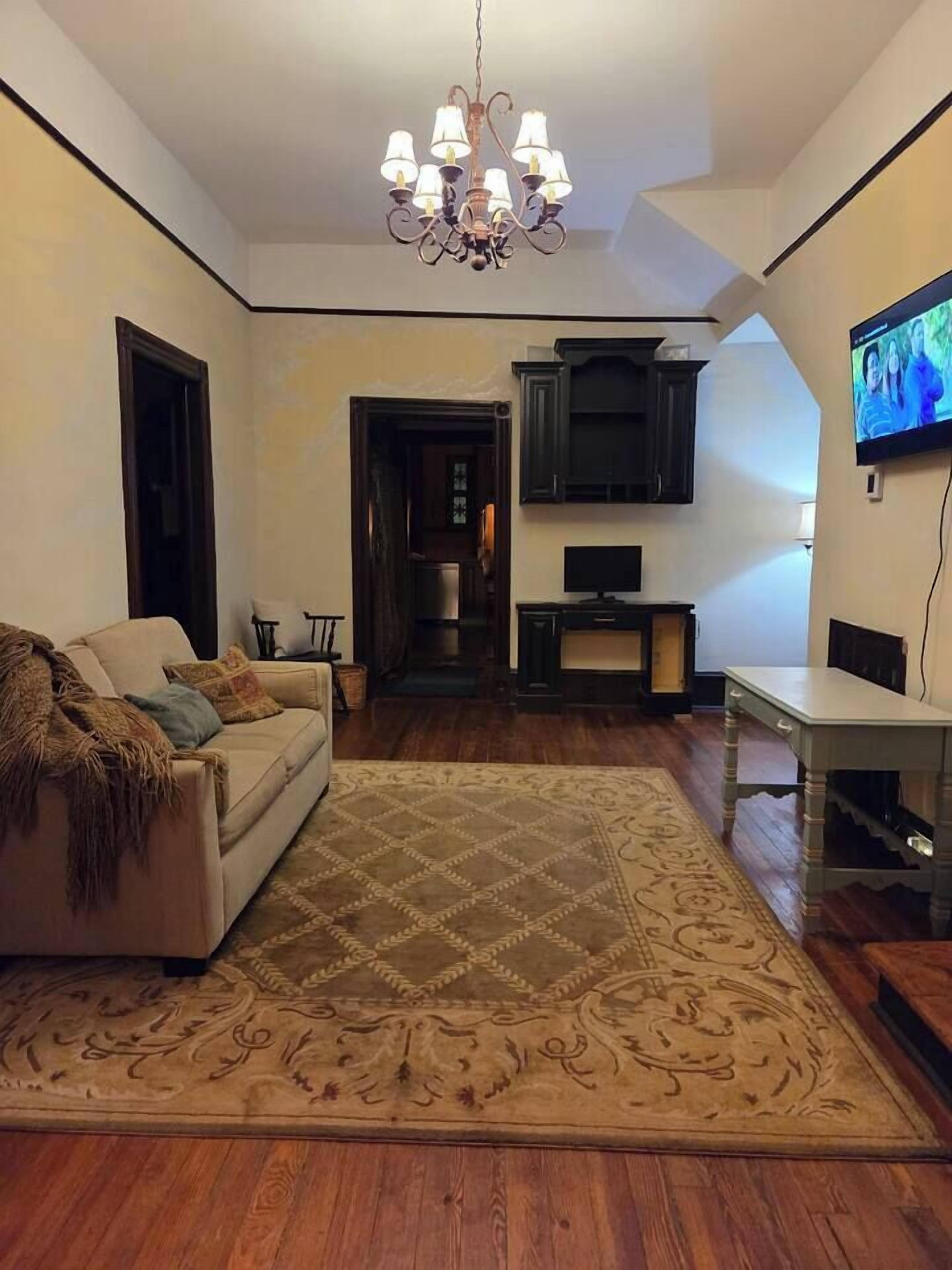 A living room with a sofa, a patterned rug, a chandelier, a television, and a cabinet.