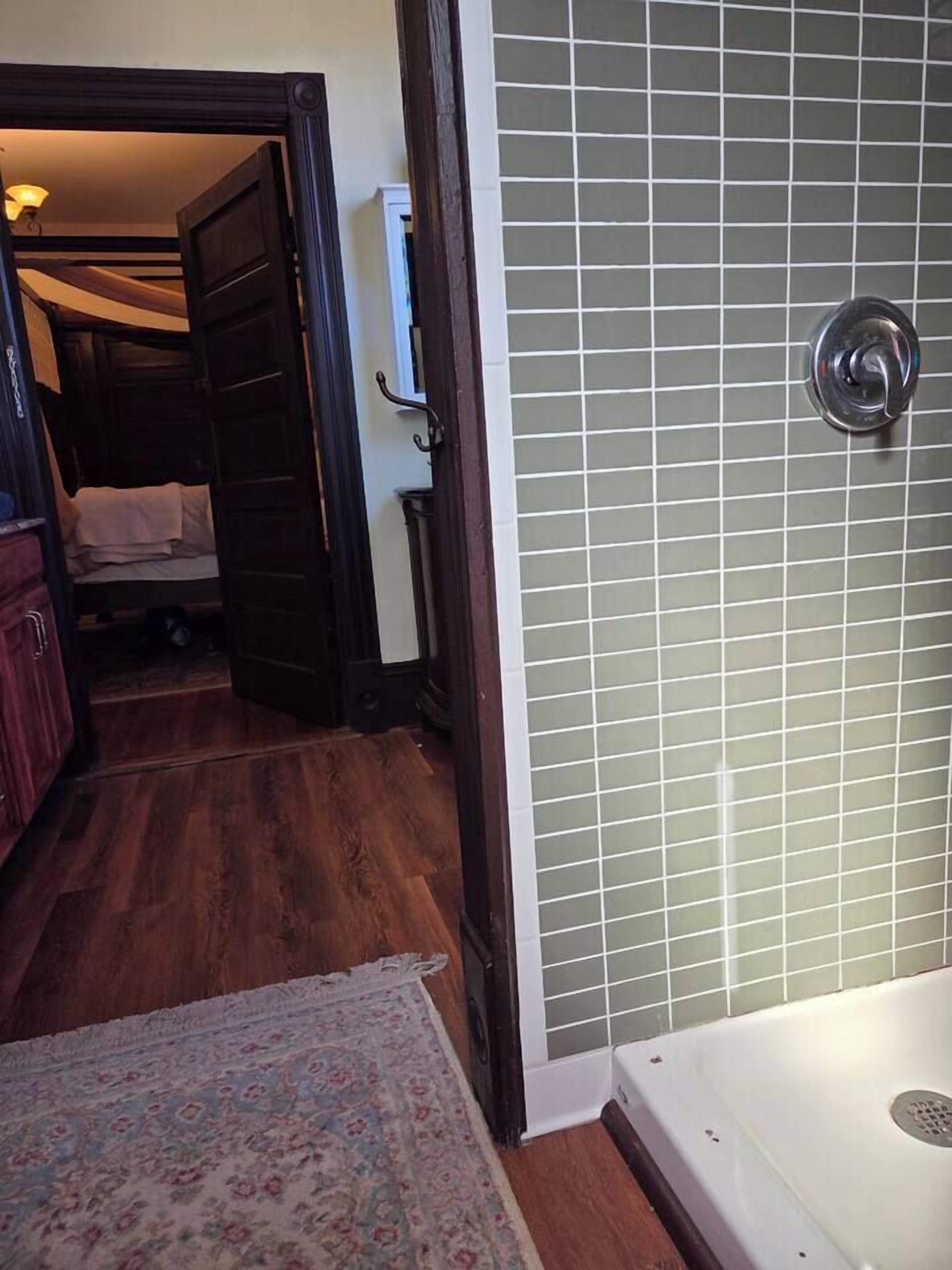Ein Badezimmer mit gefliesten Duschwänden, einer weißen Badewanne und Holzboden.