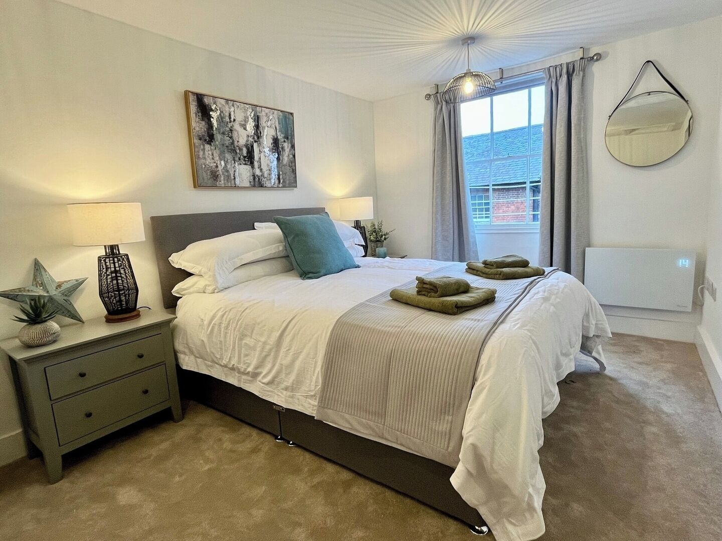 A neatly arranged bedroom with a bed, bedside tables, a lamp, a star decoration, a painting, and a window with curtains.