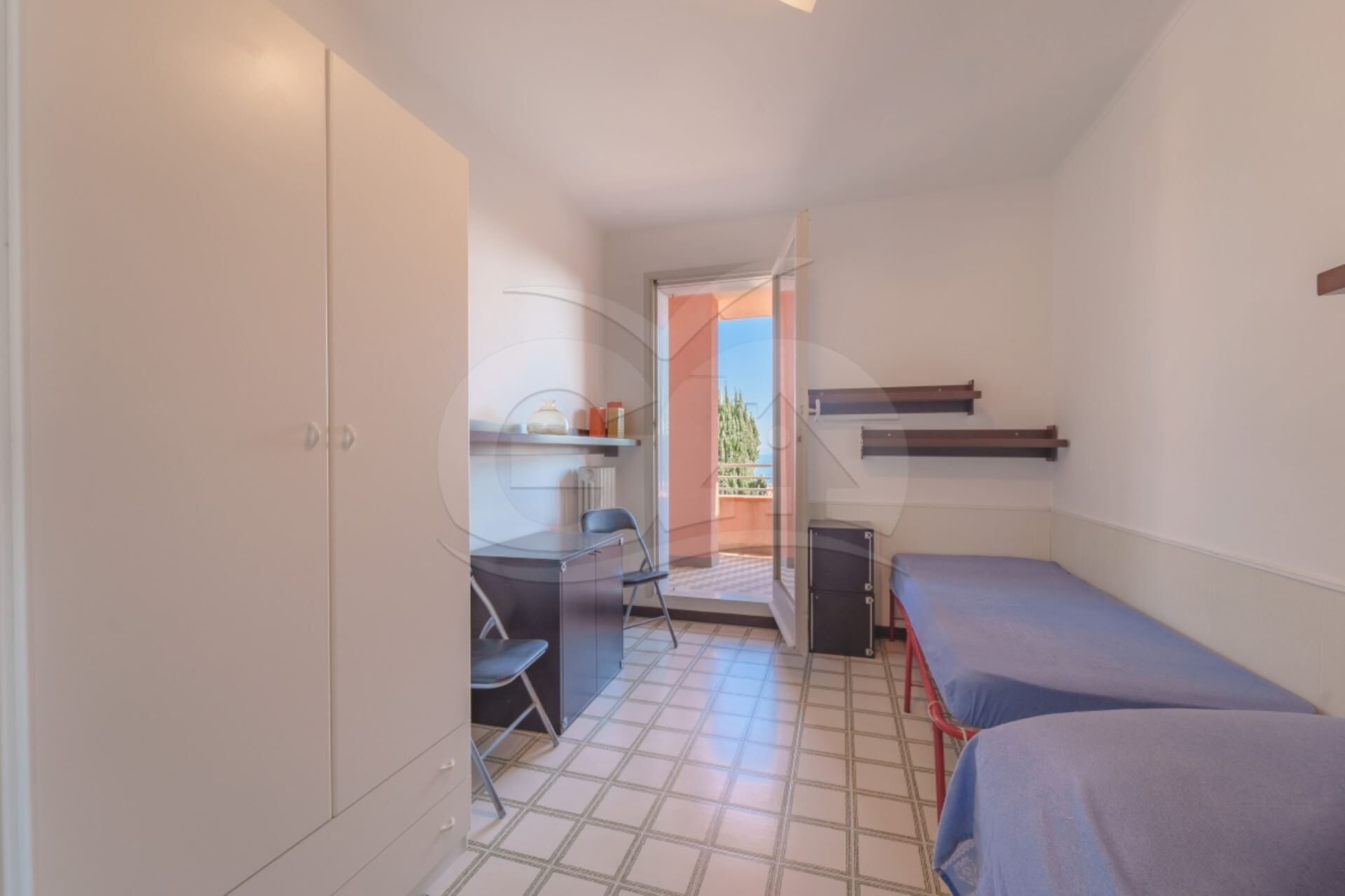 A small, compact room with a kitchenette, a desk, and two single beds.