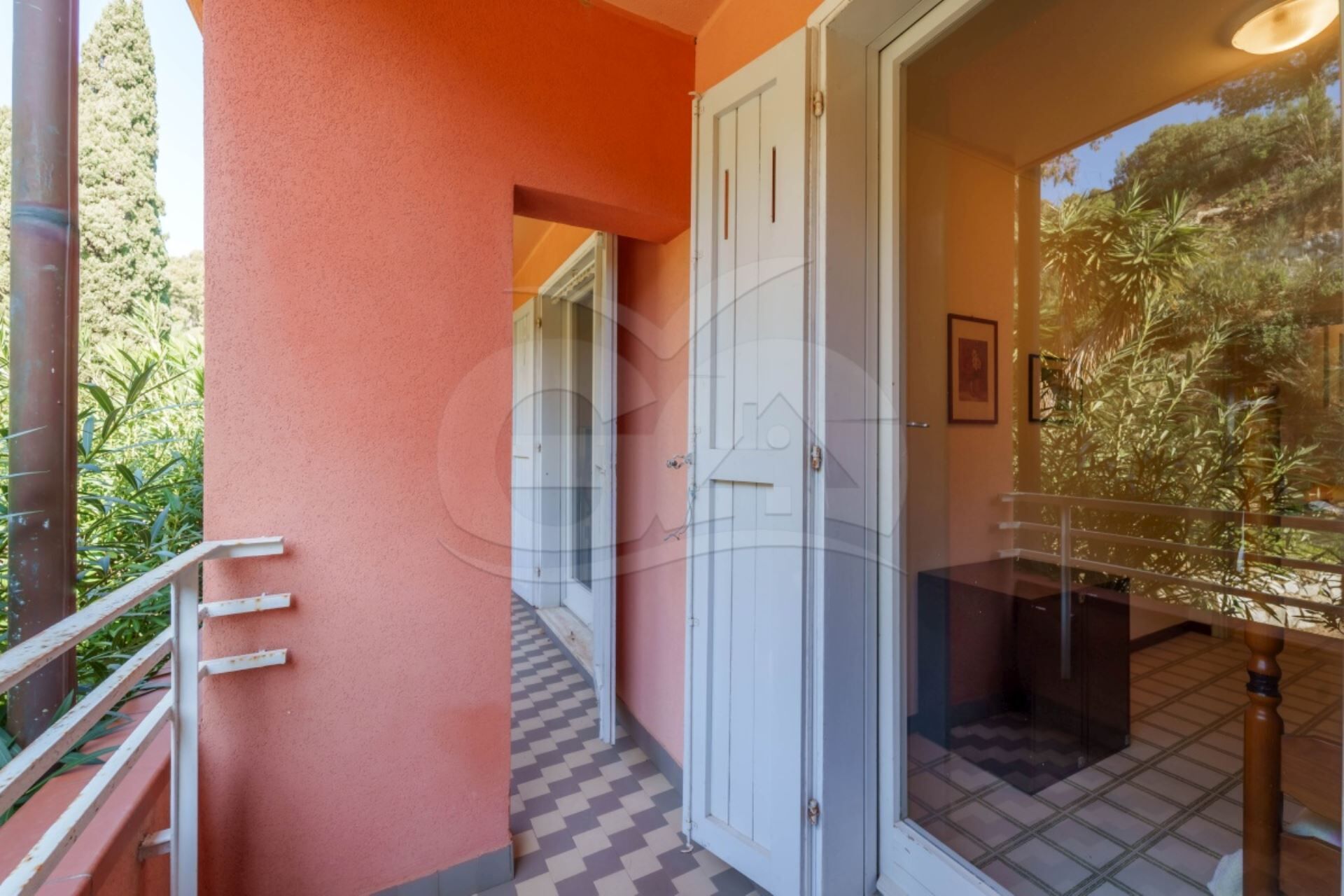 A corridor with a checkered floor, a glass door, and a balcony with a railing.