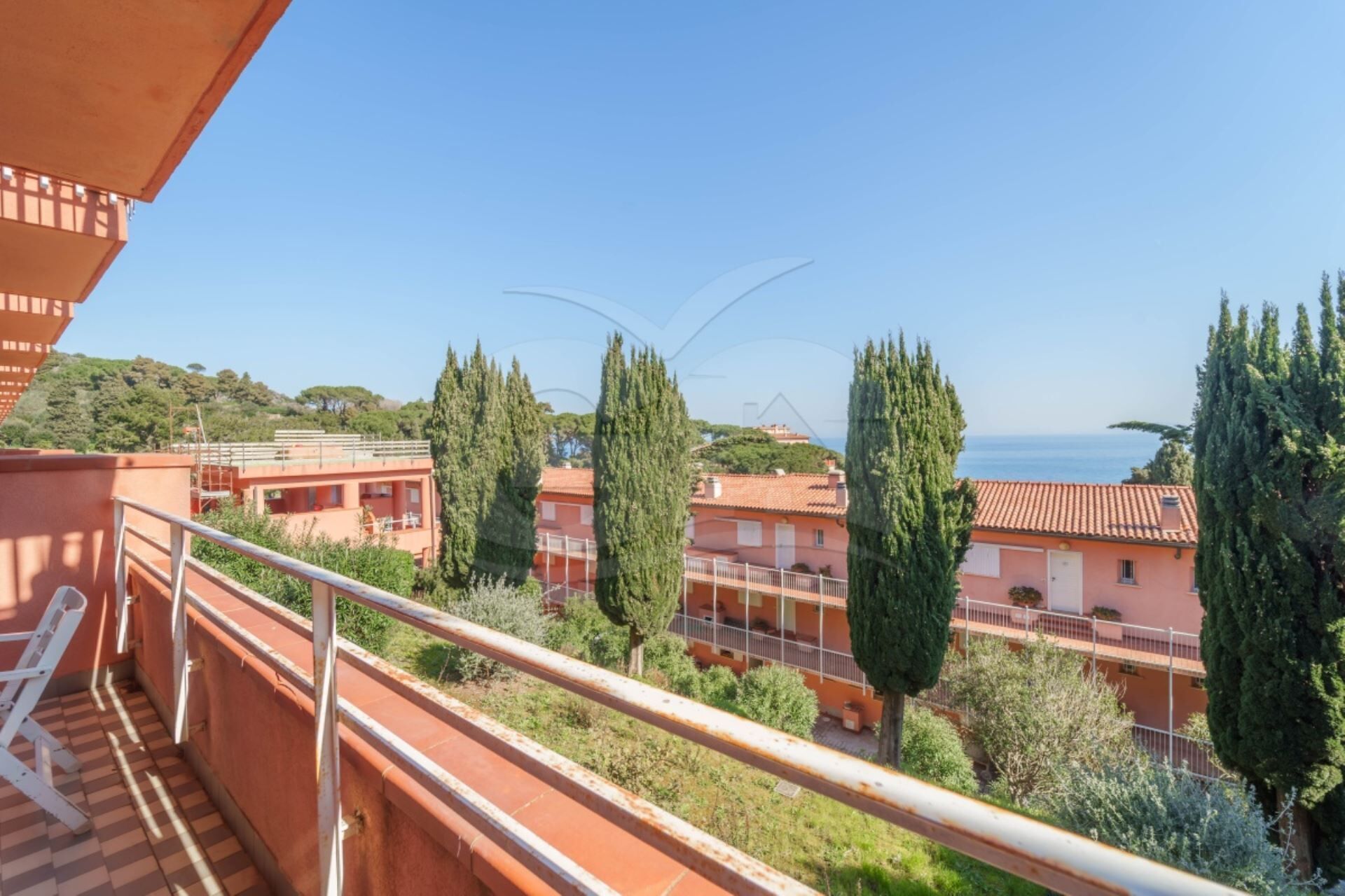 A balcony with a view of terraced houses, cypress trees, and a clear blue sky.