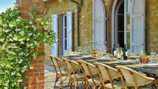An outdoor dining area with wicker chairs and a table set for a meal, overlooking a stone building with arched windows. - Villa Teresina - Guardistallo, Pisa (Guardistallo)