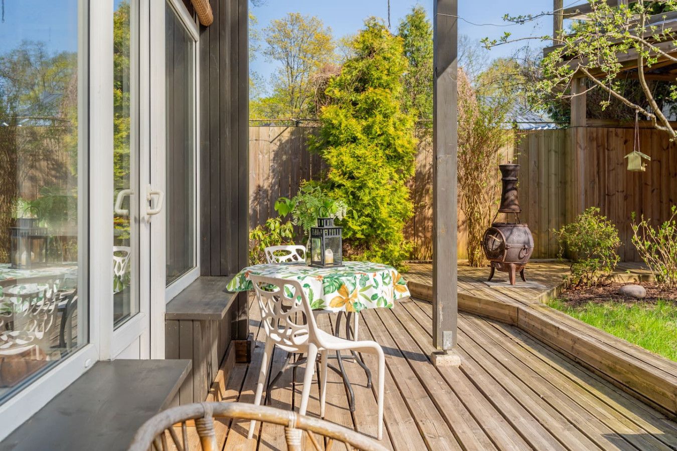 A wooden deck with a table and chairs, a barbecue grill, and a garden area with trees and plants.