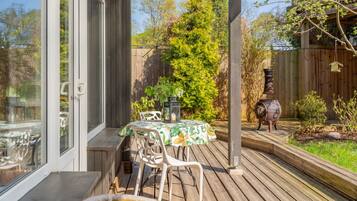 A wooden deck with a table and chairs, a barbecue grill, and a garden area with trees and plants.