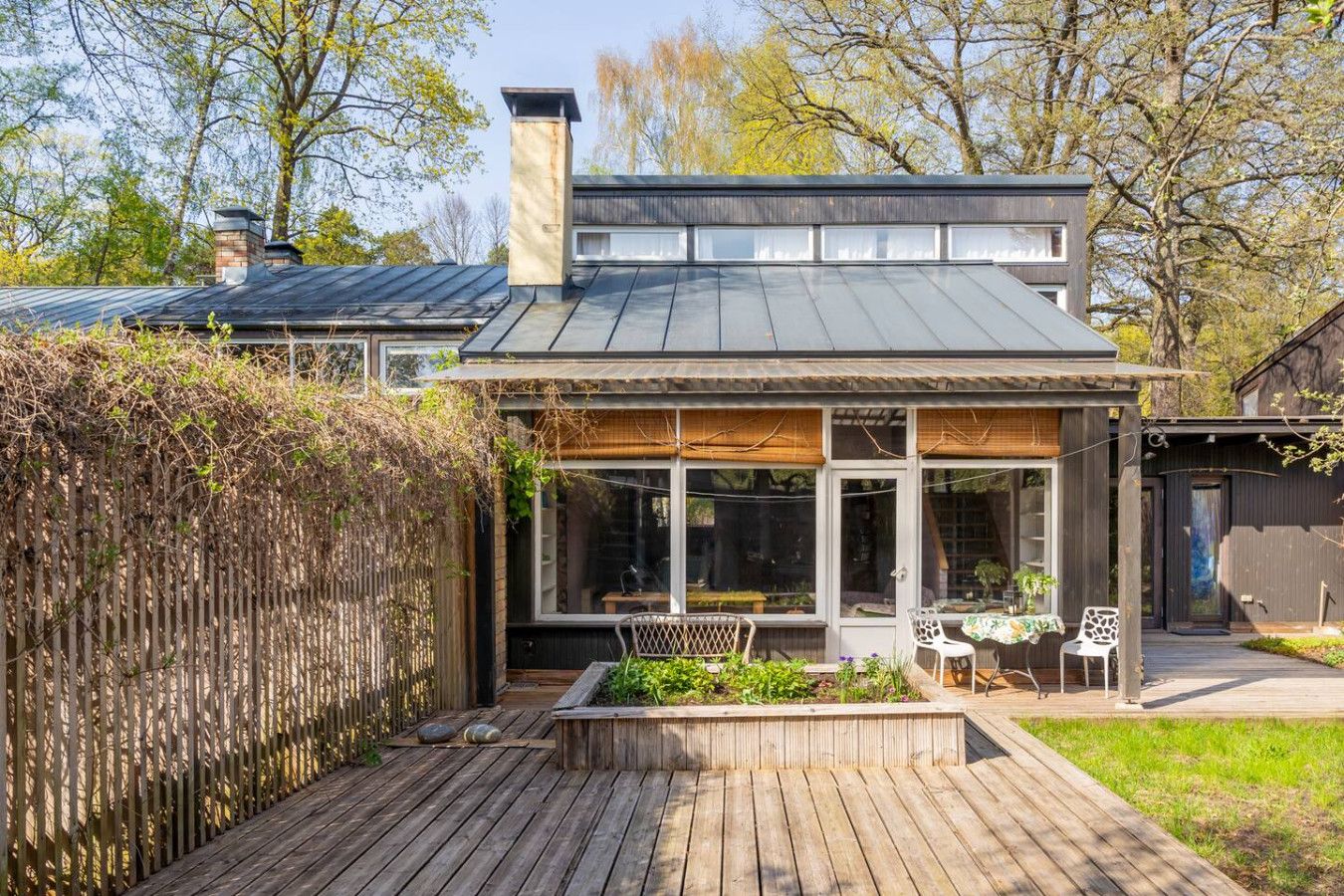 A modern house with a large glass conservatory, wooden deck, and a garden area.