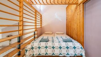 A bedroom with a wooden slatted ceiling, a bed with a patterned quilt, and a wall-mounted projector.