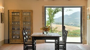 Un comedor con una mesa y sillas, un armario de madera con vajilla, y un ventanal con vistas al campo.
