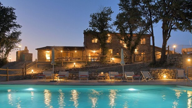 Zona junto a la piscina con sillones de descanso y un edificio de piedra con múltiples ventanas, rodeado de árboles.