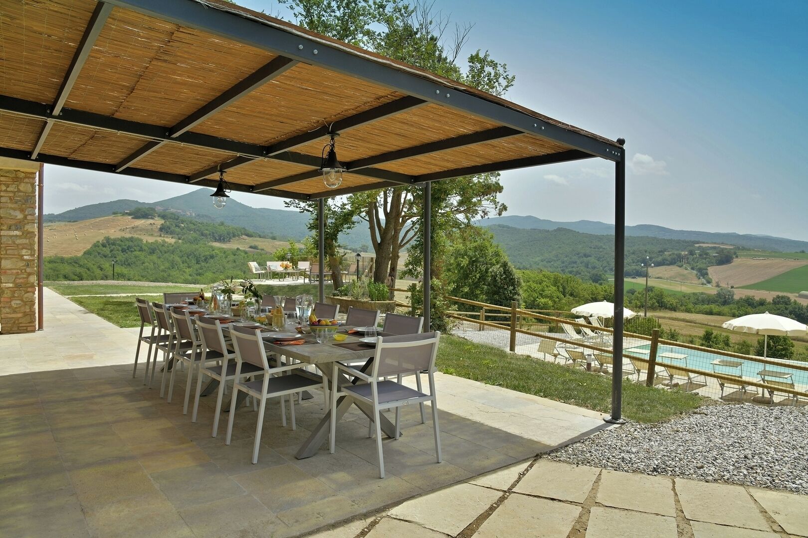 An outdoor dining area with a table set for six, overlooking a pool and scenic hills.