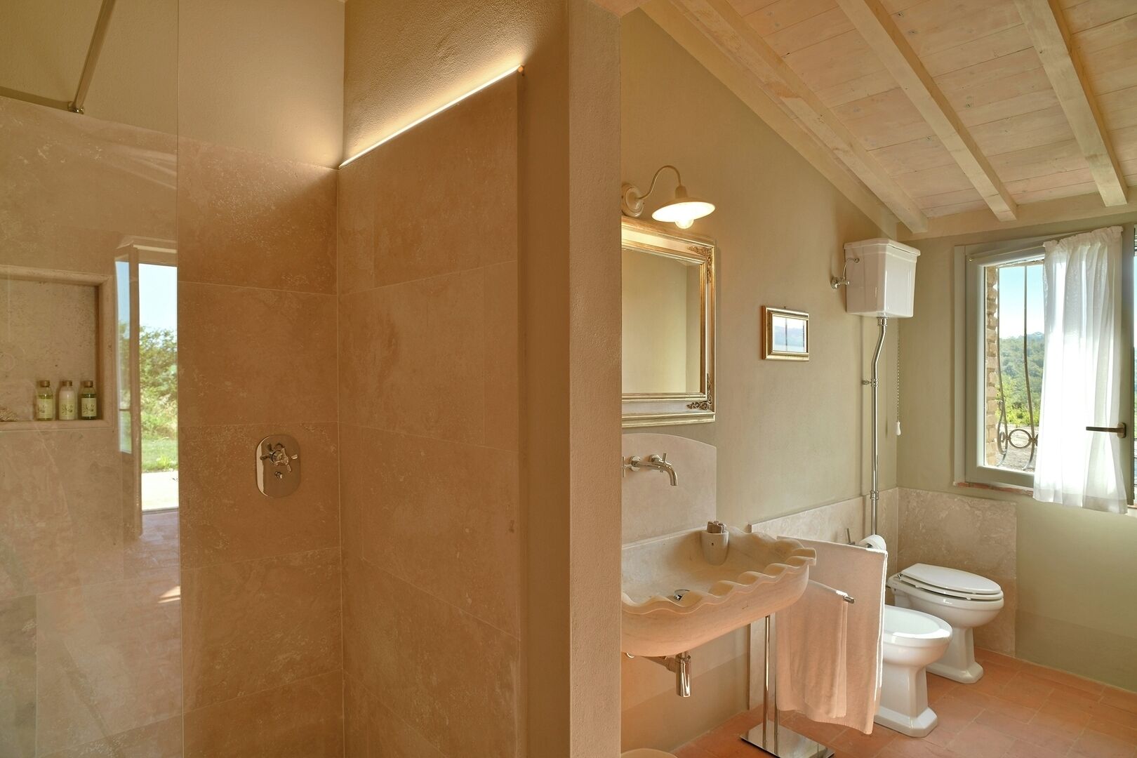 A bathroom with a shower, two sinks, a toilet, and a window with curtains.