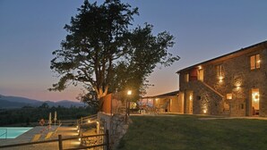 Edificio de piedra con piscina y un gran árbol en primer plano.