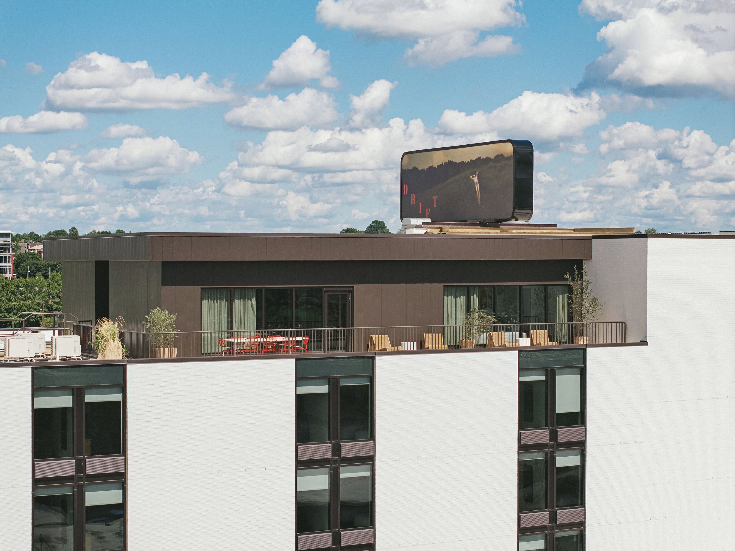 Un bâtiment moderne doté d’un toit plat, de grandes fenêtres et d’un balcon avec un espace salon extérieur.