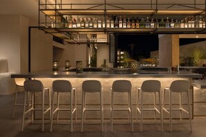 Sip crafted drinks at the glowing bar beneath bottle displays. - Boutique Stay with Cozy Fire Pits, Poolside Dining & Scenic Views (Palm Springs)