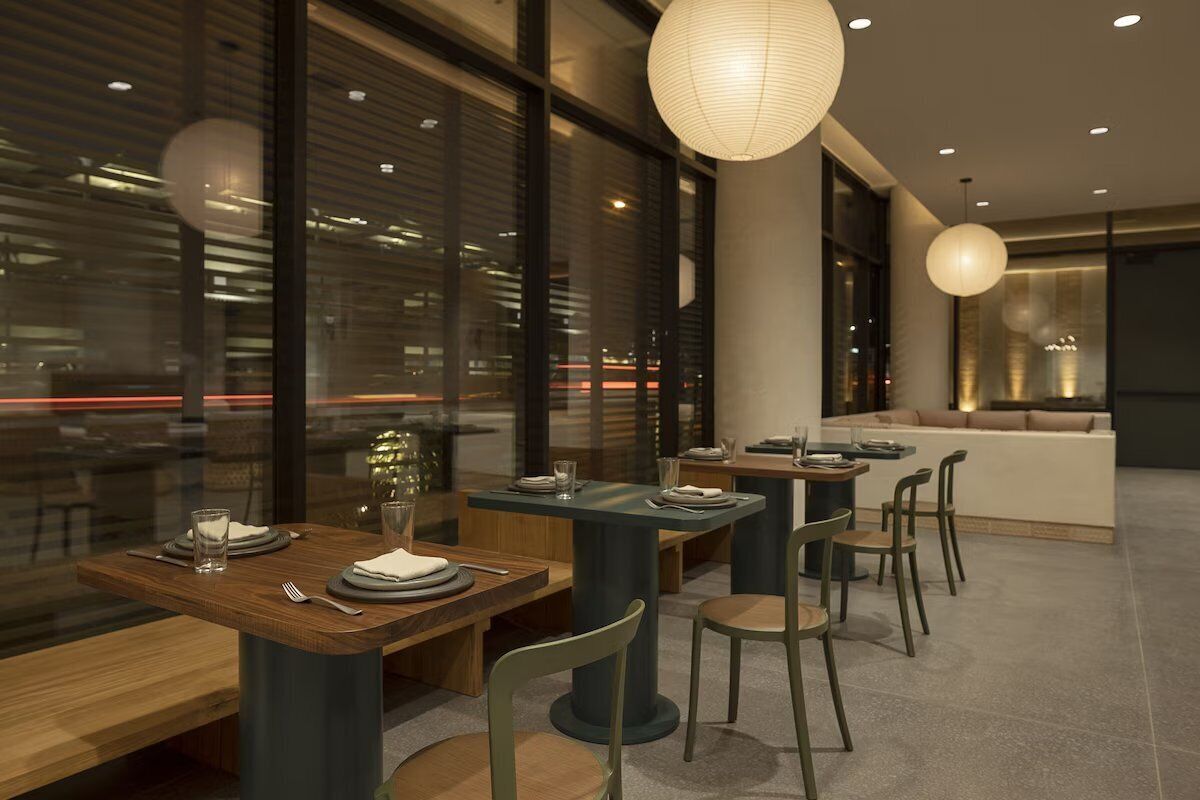 A modern dining area with tables and chairs, large windows, and pendant lighting.