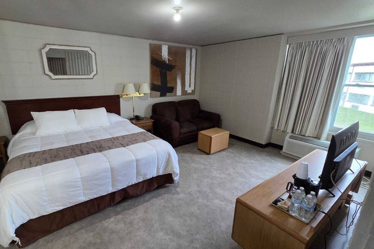 A hotel room with a large bed, a sofa, a desk with a TV, and a window with curtains.