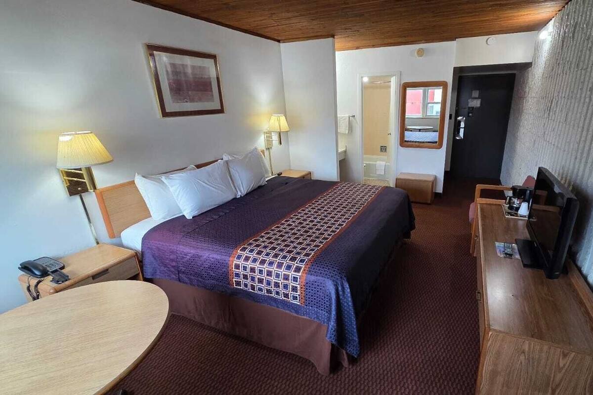 A hotel room with a bed, bedside tables, a desk, a chair, a TV, and a door.
