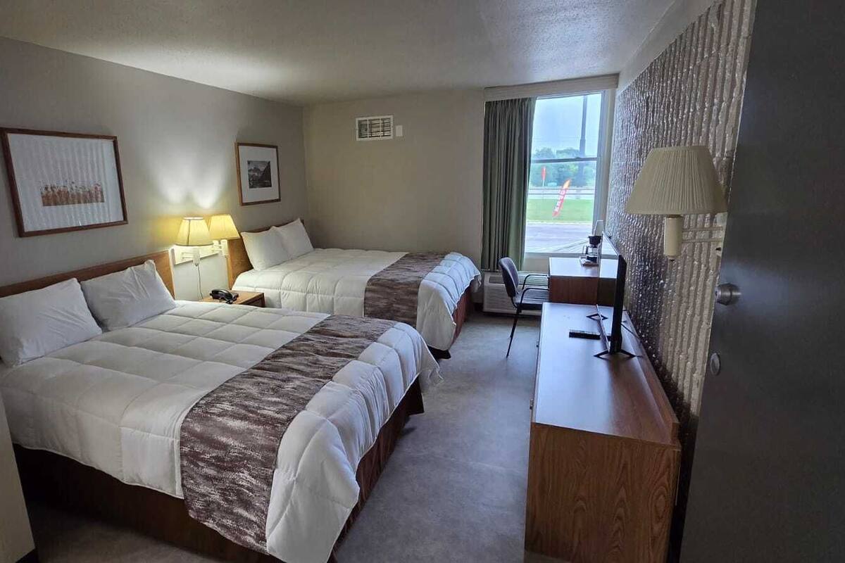 A hotel room with two beds, a desk, a chair, a lamp, and a window with curtains.