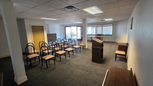 Un salón de conferencias con filas de sillas, un atril y ventanas amplias.