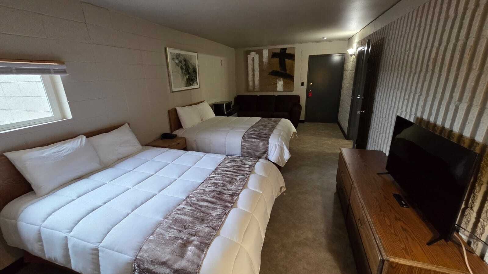 Habitación de hotel con dos camas, un televisor y una puerta que da a un pasillo.